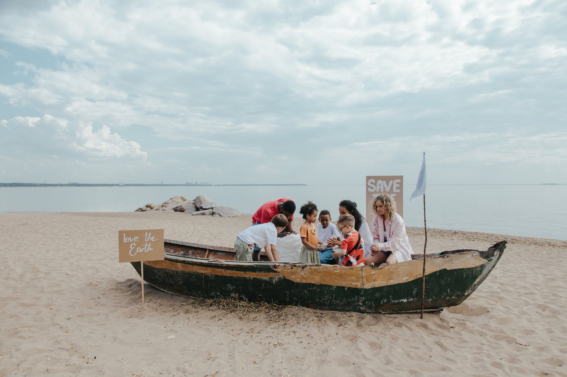 Kids in a boat on the beach with signs that say "save the earth"